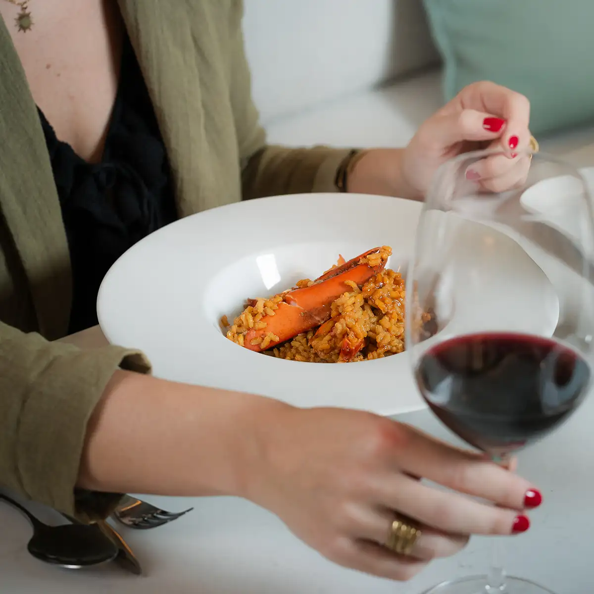 Persona sirve comida en plato blanco con vino en mesa.