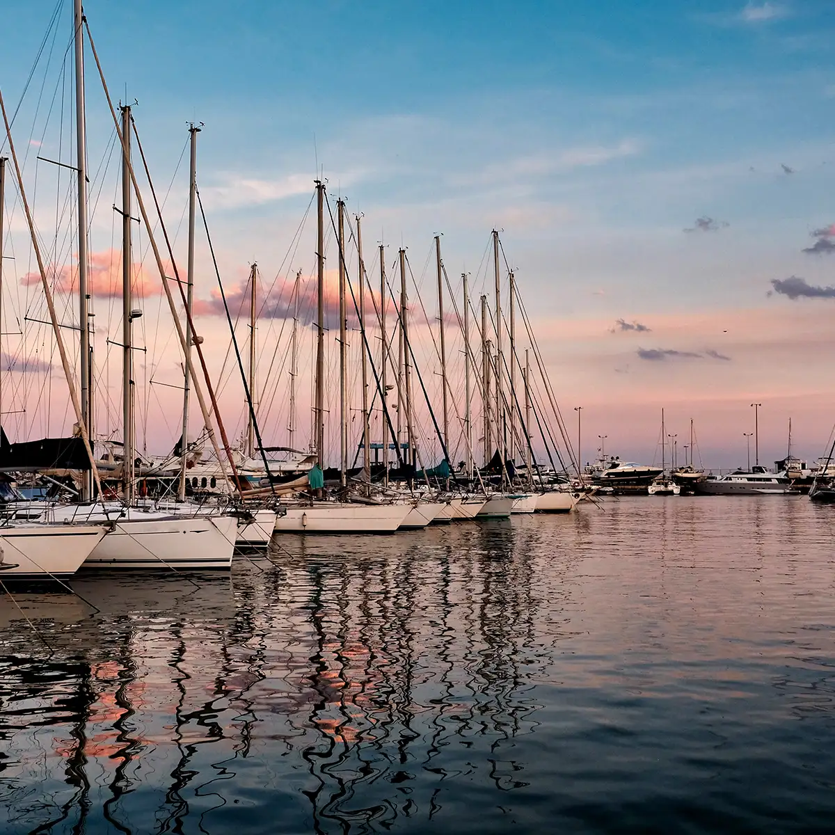 Barcos y velas amarrados en un puerto al atardecer, reflejados en el agua