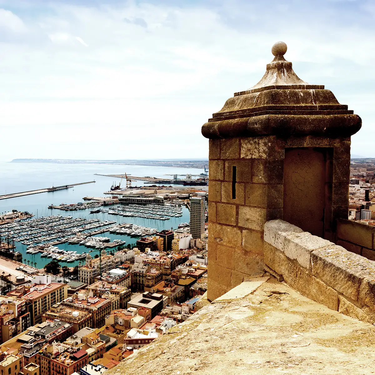 Mirador de piedra con vista a un puerto lleno de barcos y ciudad costera