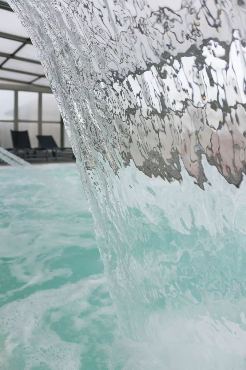 Cortina de agua cayendo en piscina interior con cielo claro y sillas al fondo