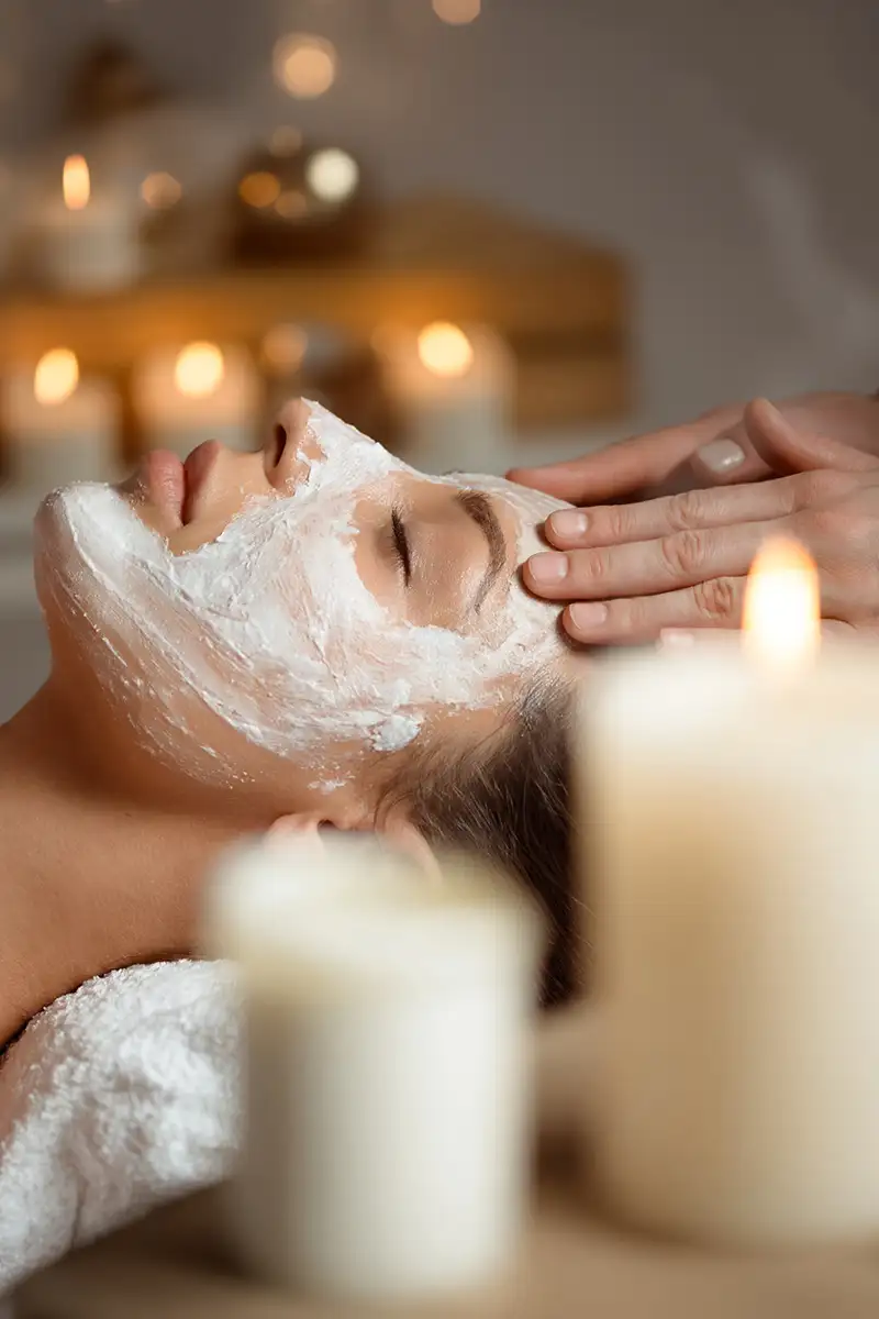 Masaje facial con mascarilla de espuma, manos aplicando y piel relajada