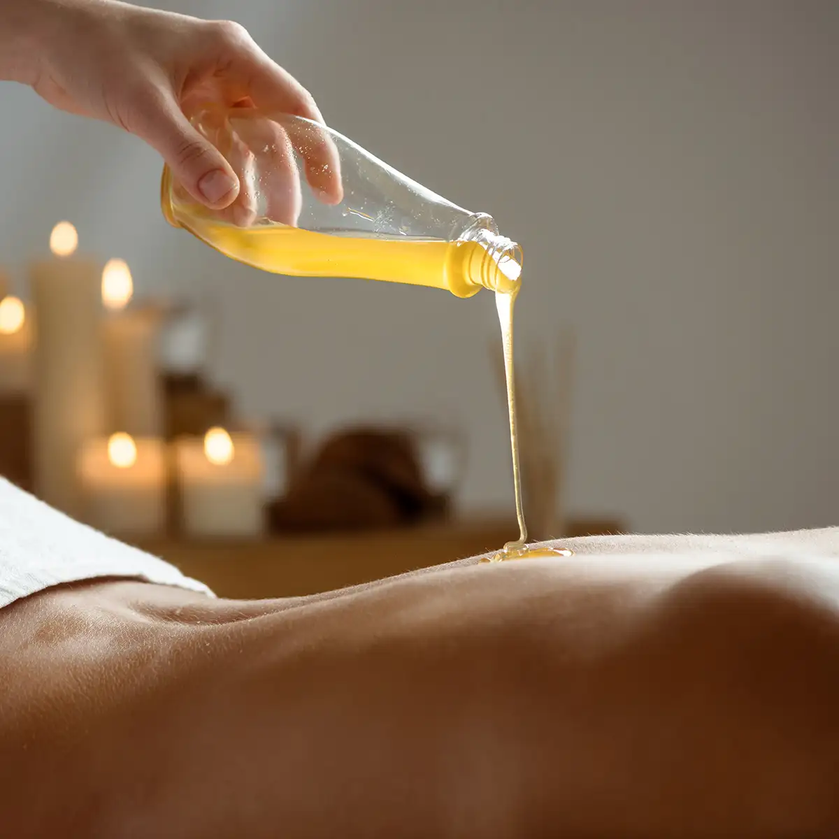 Mano sostiene botella y vierte aceite amarillo sobre la piel de un brazo