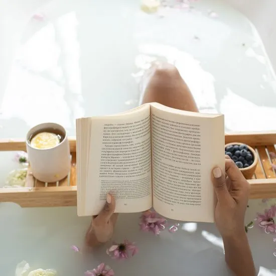 Persona leyendo un libro abierto sobre mesa con t&eacute; y frutas.