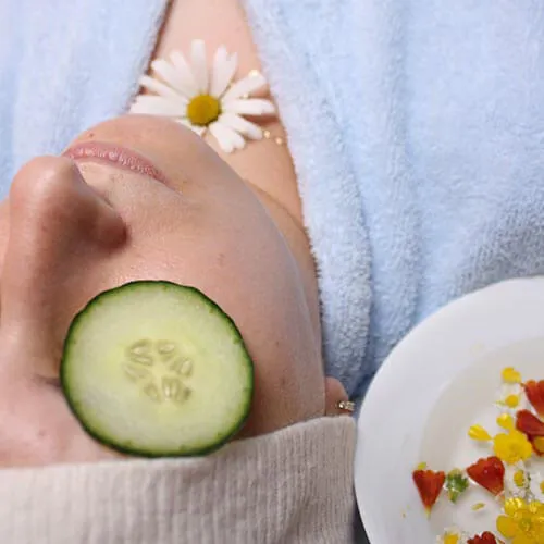 Rostro relajado con rodaja de pepino y flor blanca, tratamiento facial.