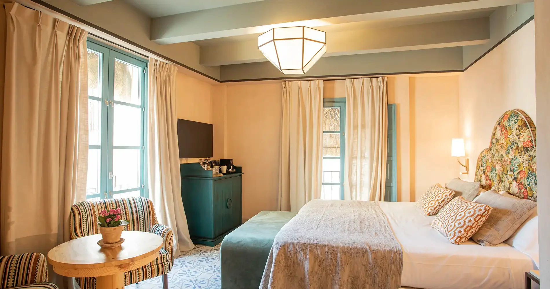 Dormitorio luminoso con cama, cortinas beige y l&aacute;mpara colgante geom&eacute;trica