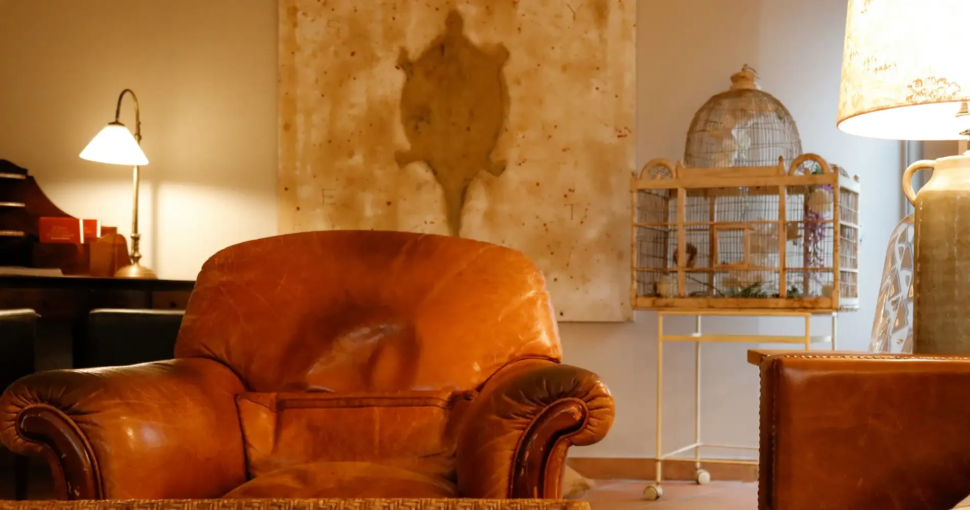Sala de estar con sill&oacute;n de cuero, jaula decorativa y luces c&aacute;lidas.