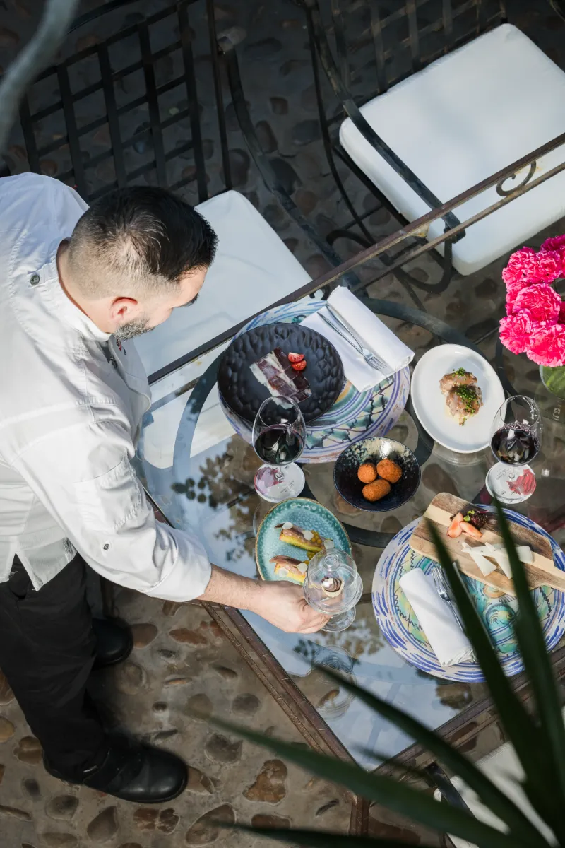 Cocinero sirve platos en mesa al aire libre con vino y decoraci&oacute;n roja