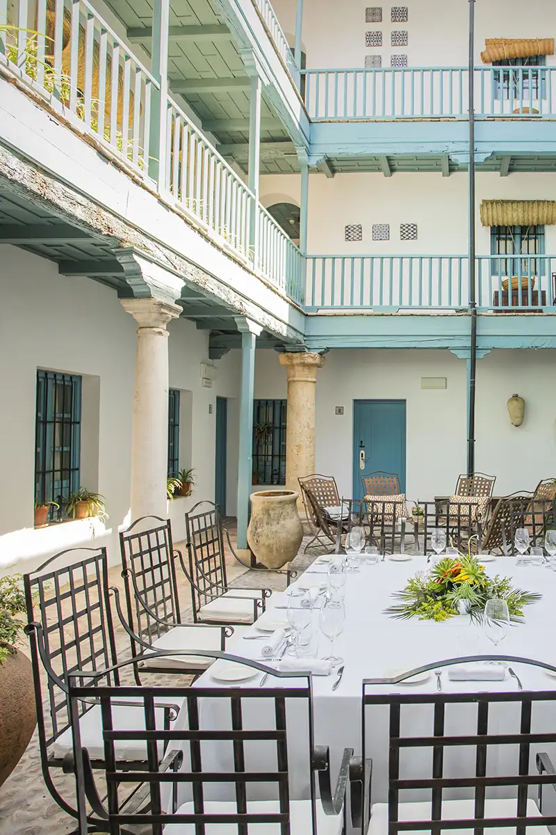 Patio andaluz con mesas servidas y sillas, columnas y arquitectura colonial azul