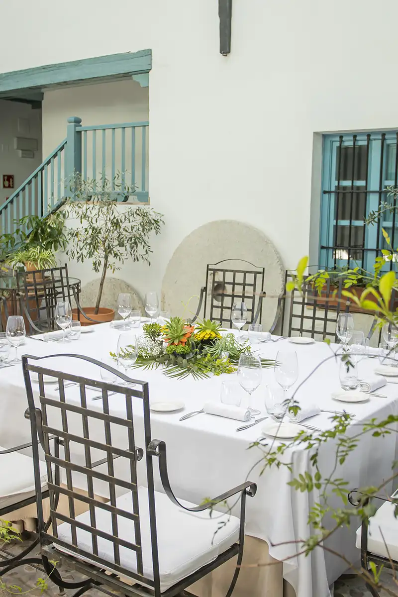 Mesa decorada con sillas de madera, vajilla y flores en un patio.