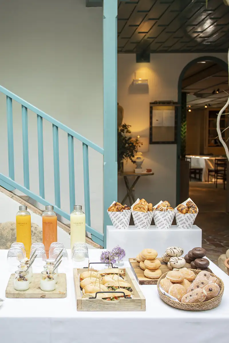 Mesa de desayuno con boller&iacute;a, botellas y ambiente en terraza interior