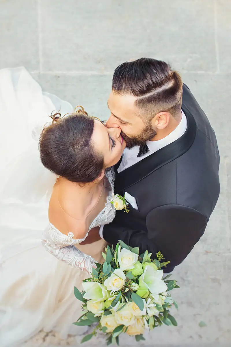Novios bes&aacute;ndose, ella con vestido blanco y ramo de flores verdes y blancas