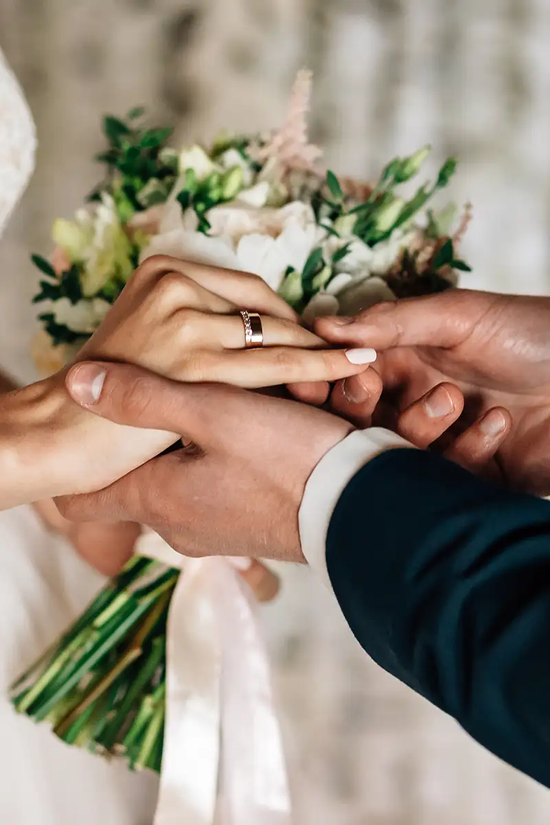 Manos uniendo anillos con flores verdes y blancas, en celebraci&oacute;n nupcial