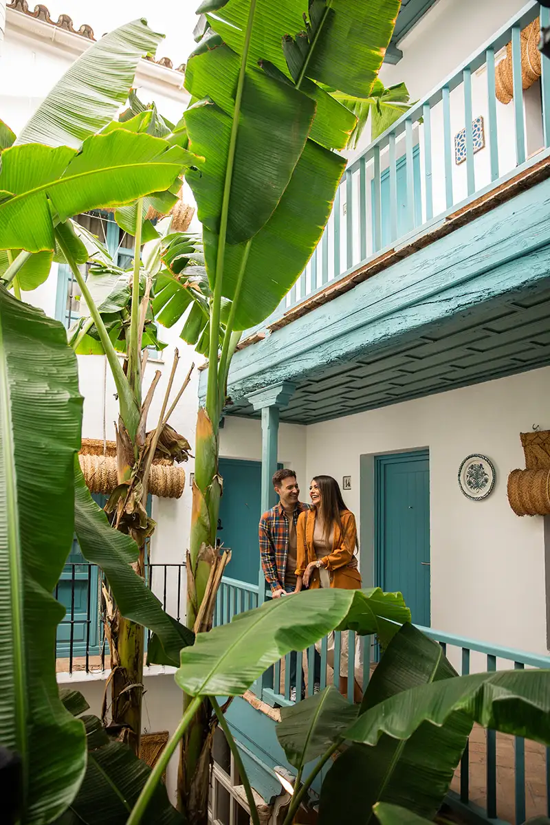 Pareja junto a casa azul, bajo grandes hojas de pl&aacute;tano verdes.