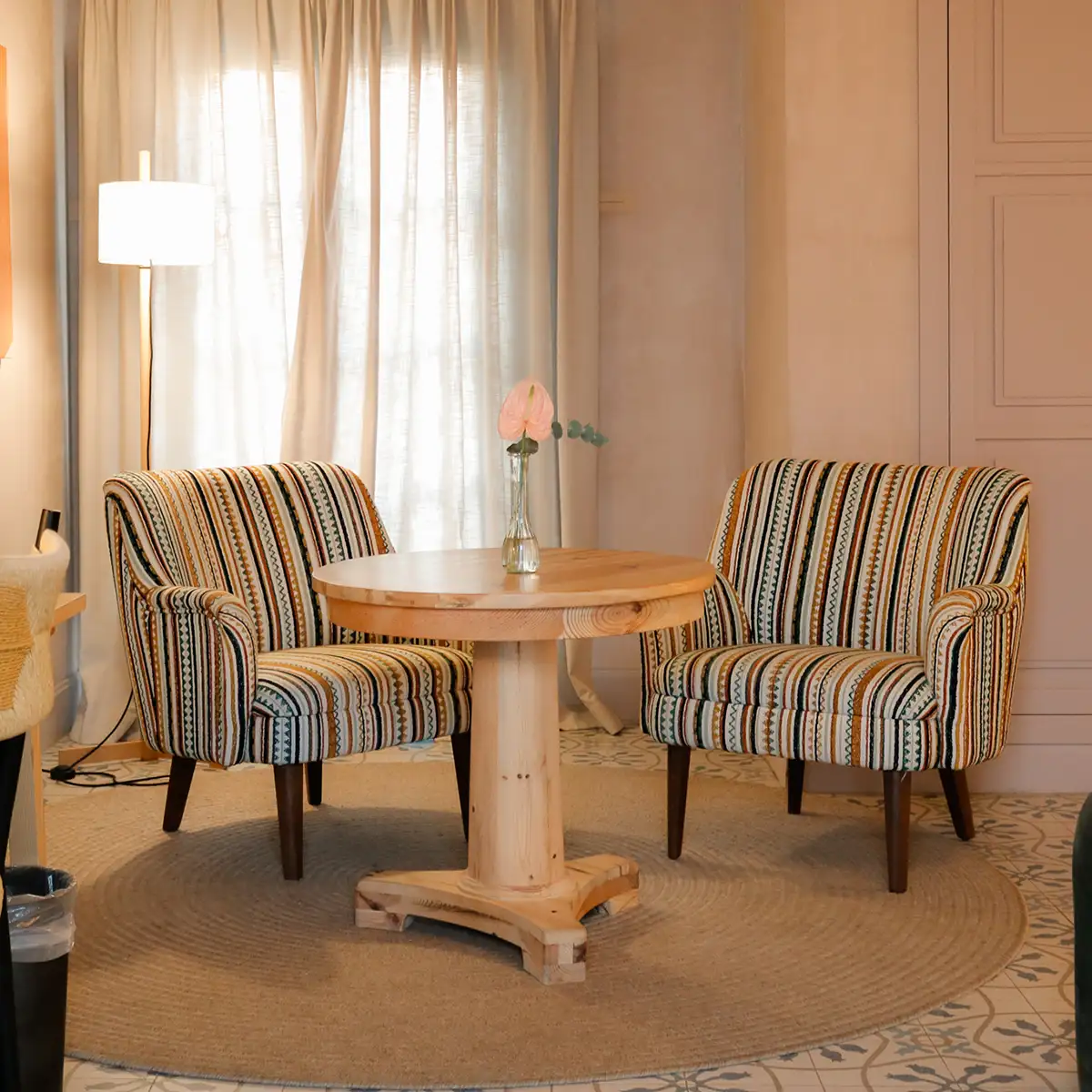 Sala con mesa redonda de madera y sillones a rayas junto a ventana