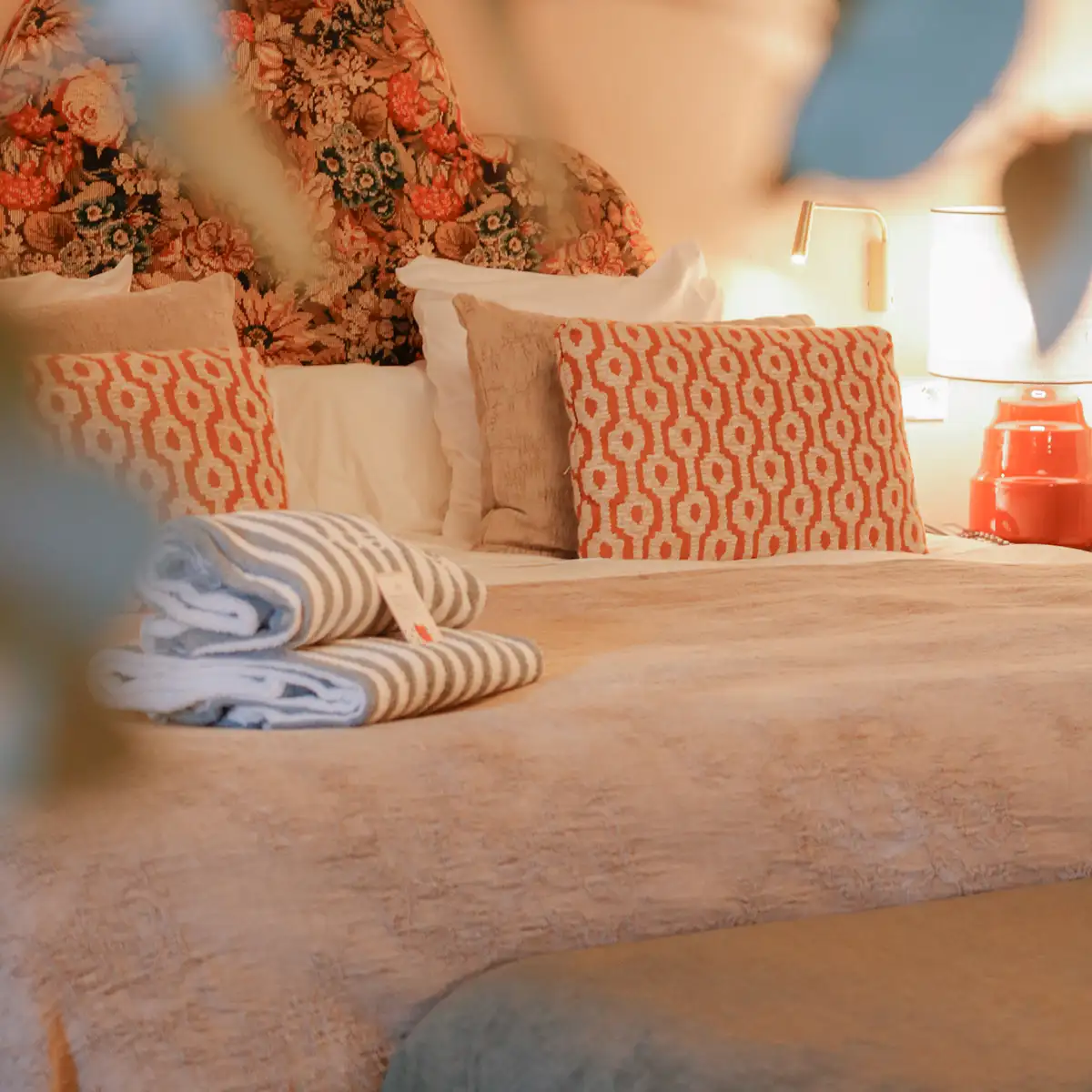 Cama con s&aacute;banas y cojines estampados, l&aacute;mpara y manta sobre una mesa.