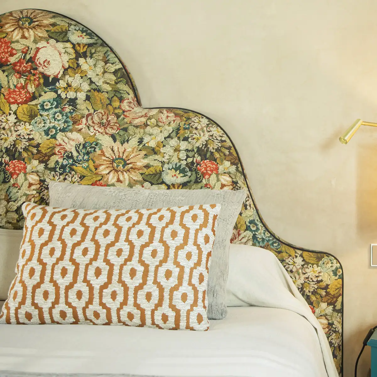 Sill&oacute;n tapizado floral con coj&iacute;n blanco y patr&oacute;n naranja, pared beige.