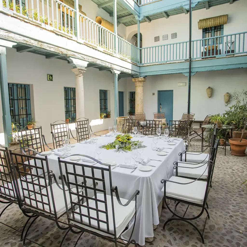 Patio andaluz con mesas y sillas met&aacute;licas, decoraci&oacute;n floral y vajilla lista