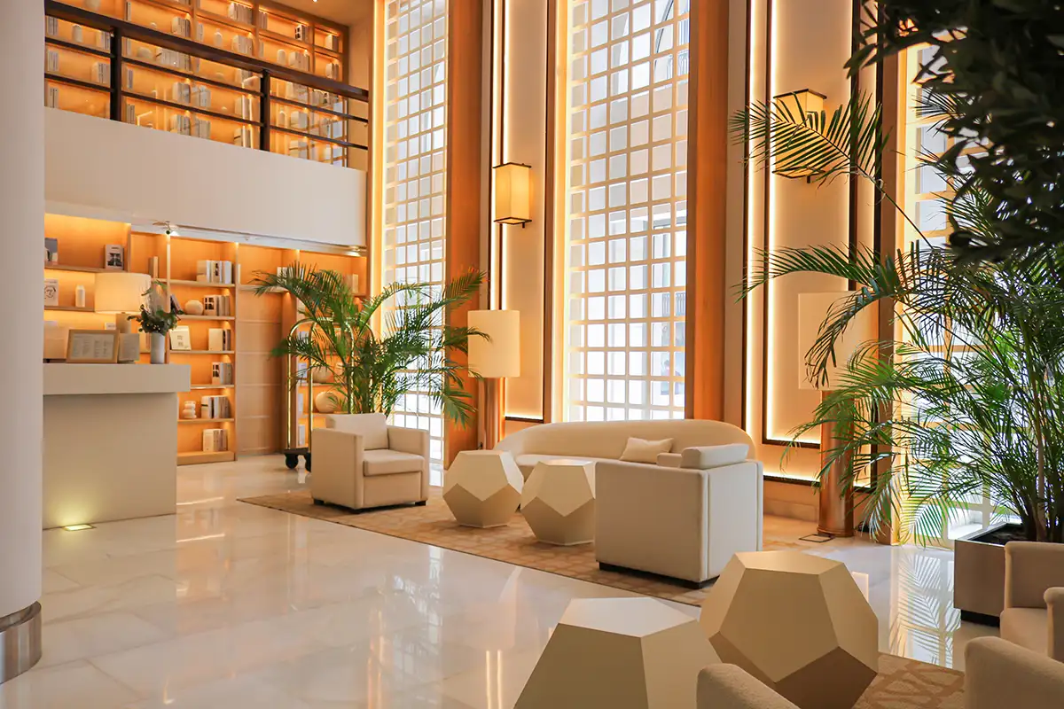 Lobby moderno con sof&aacute;s blancos, plantas y estanter&iacute;as de madera iluminadas