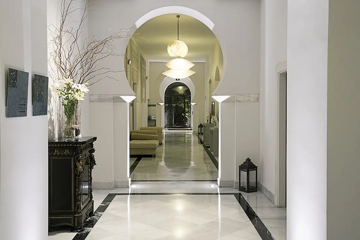 Pasillo luminoso con arcos, sillones verdes y decoraci&oacute;n floral y l&aacute;mparas colgantes