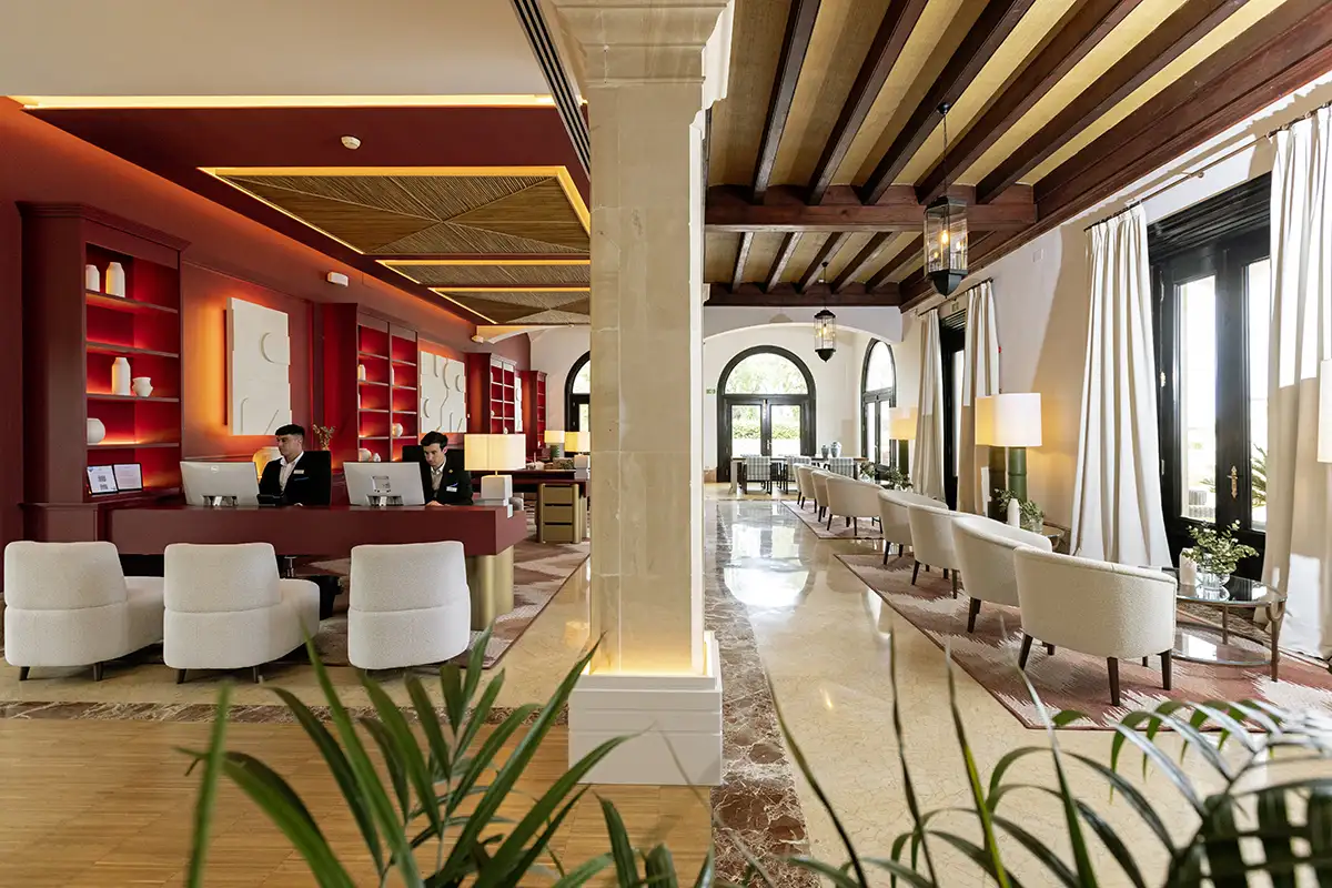 Recepci&oacute;n y sal&oacute;n de hotel con iluminaci&oacute;n c&aacute;lida y mesas con sillas blancas