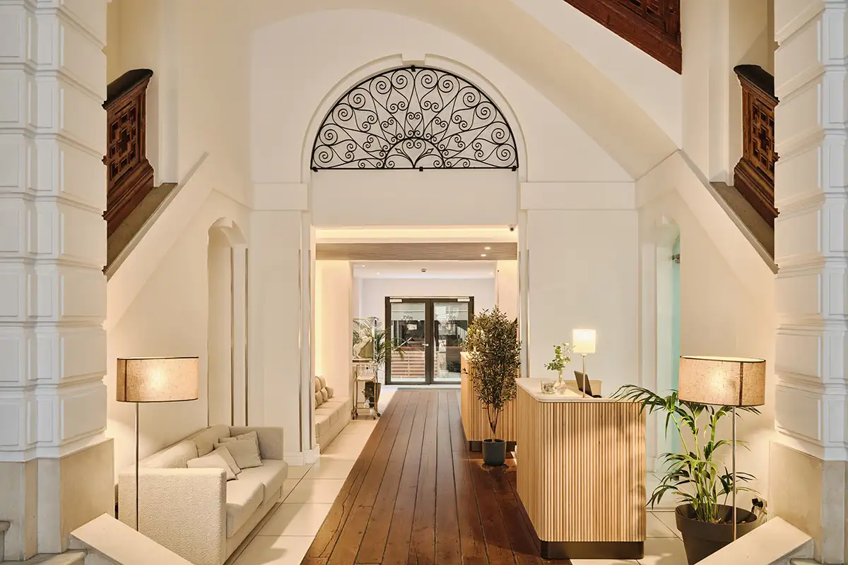 Pasillo interior luminoso con arcos blancos, panel de madera y plantas decorativas