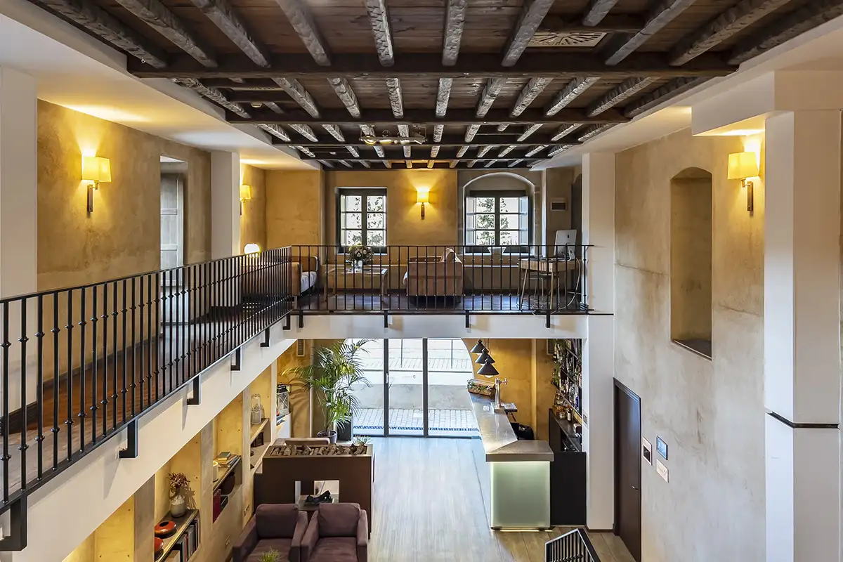 Pasillo interior con doble altura, escaleras y luz c&aacute;lida en un edificio moderno.