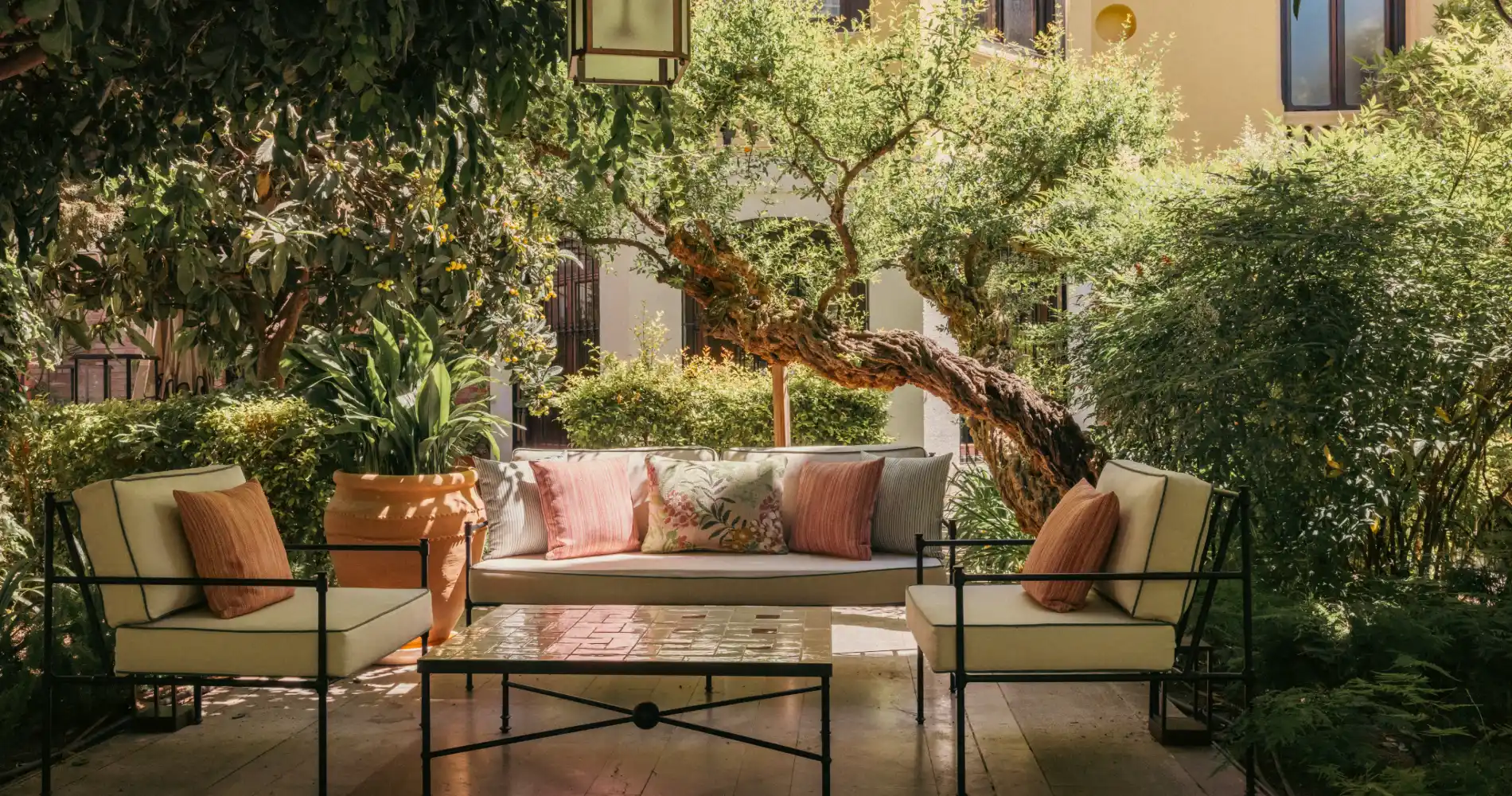 Patio con sof&aacute; y mesa de centro, rodeado de jardines y &aacute;rboles frondosos