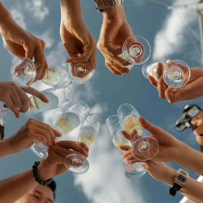 Manos brindando con vasos de cristal con bebida, al aire libre y sol