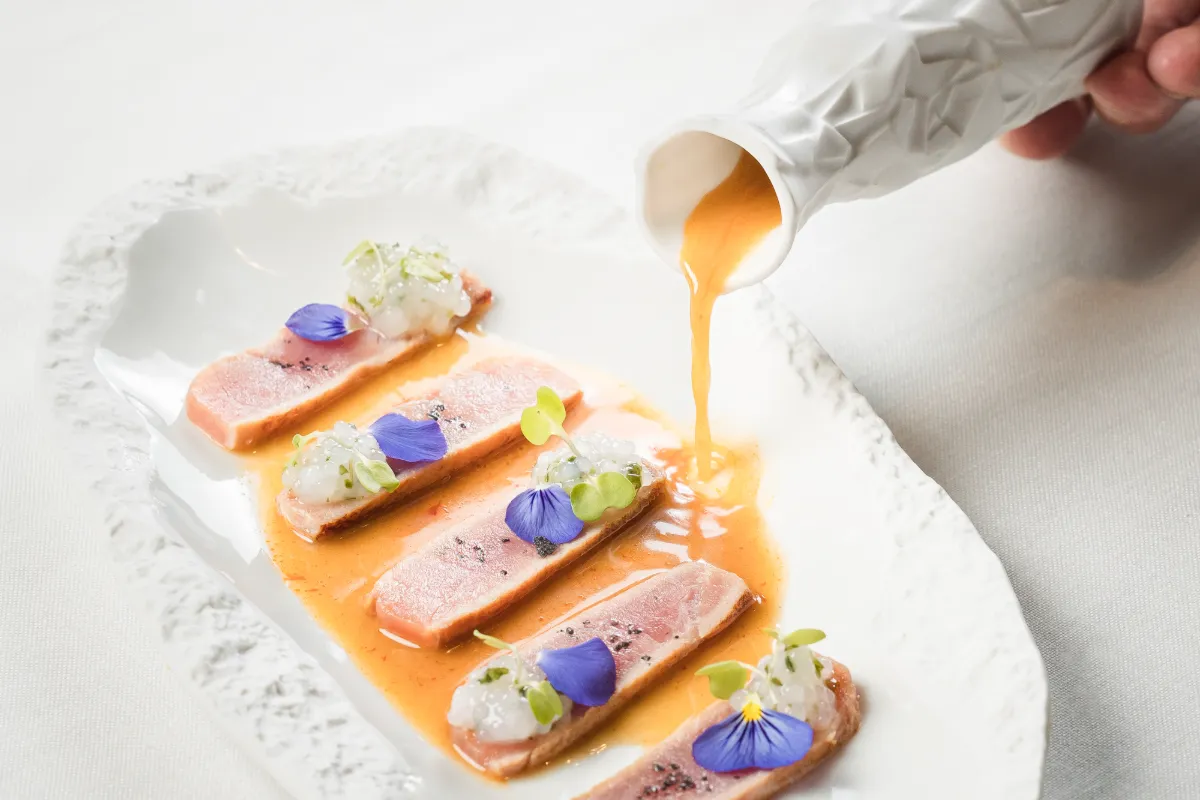 Vierte salsa naranja sobre filetes de carne con brotes y flores comestibles