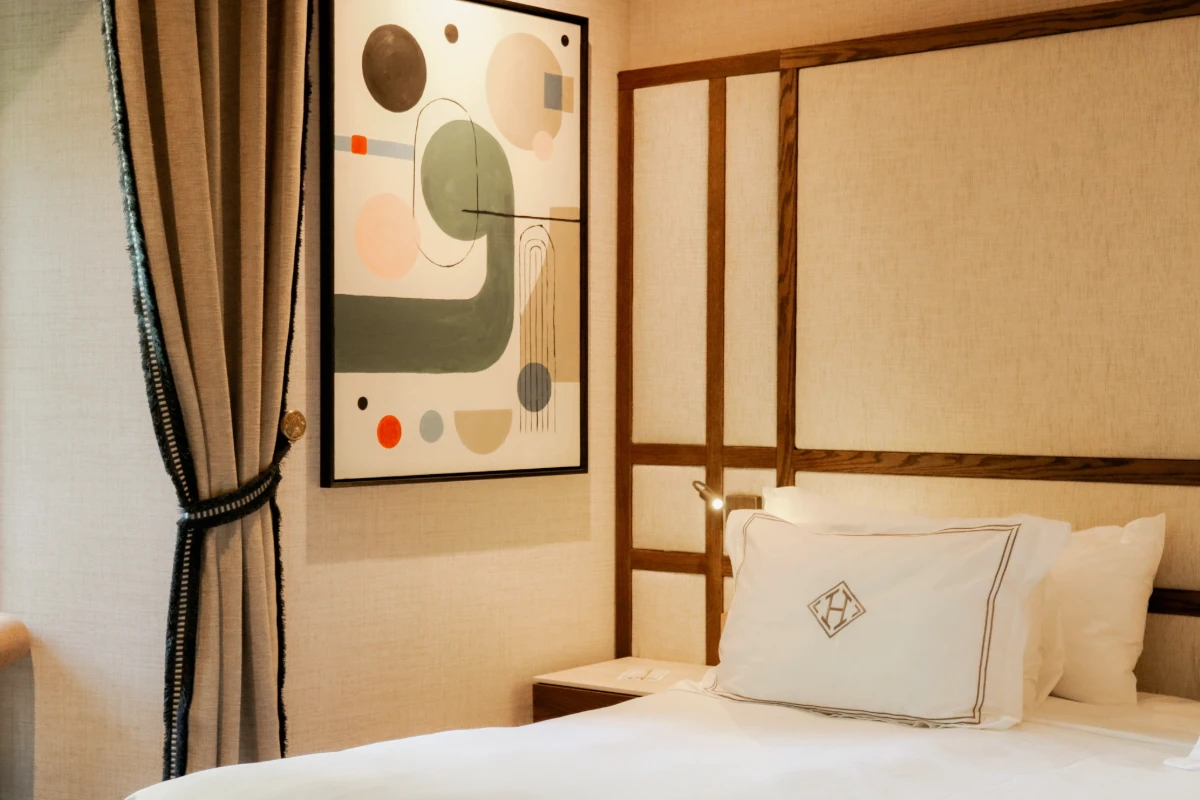 Habitaci&oacute;n con cama, cojines blancos y cuadro abstracto junto a cortinas