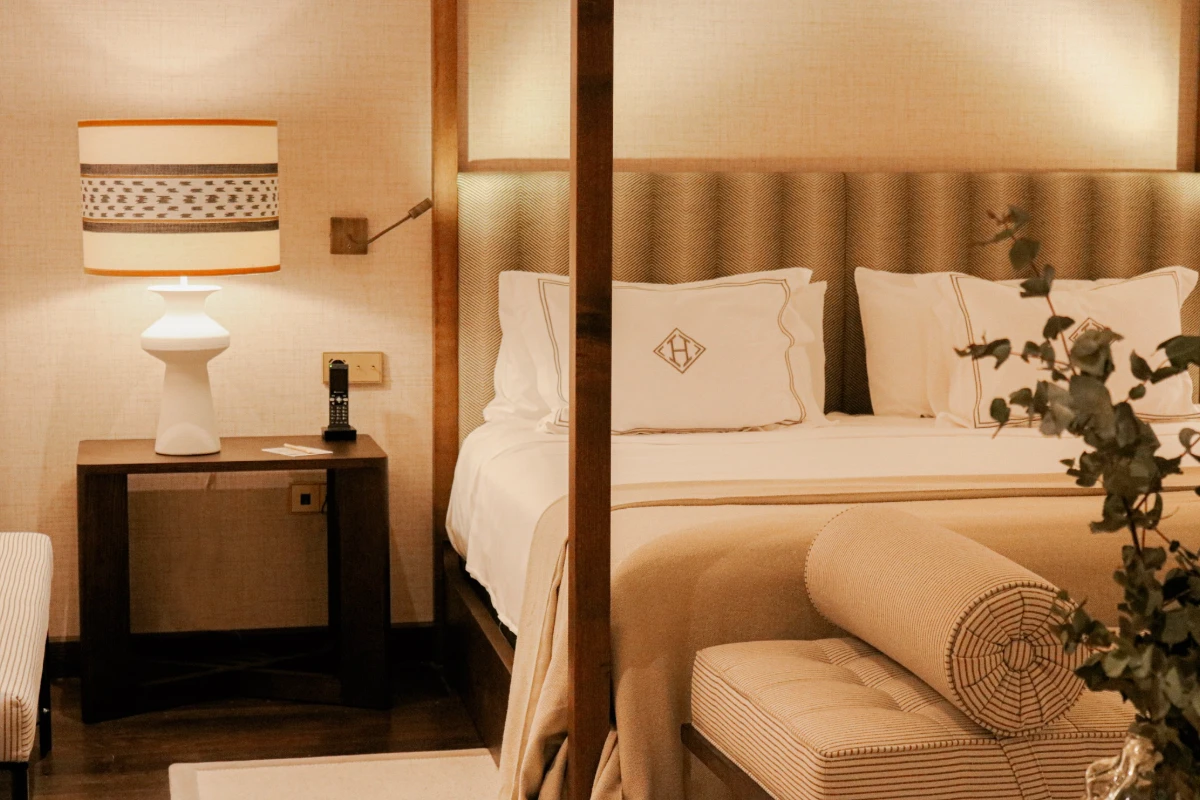 Dormitorio elegante con cama, almohadas, l&aacute;mpara y mesa auxiliar de madera