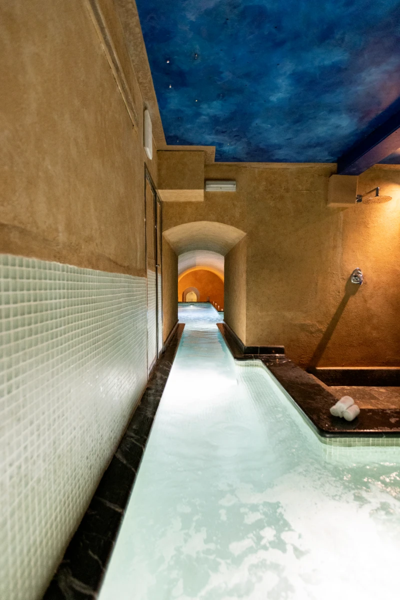 Pasillo estrecho con ba&ntilde;era de hidromasaje iluminada, en hotel o spa.