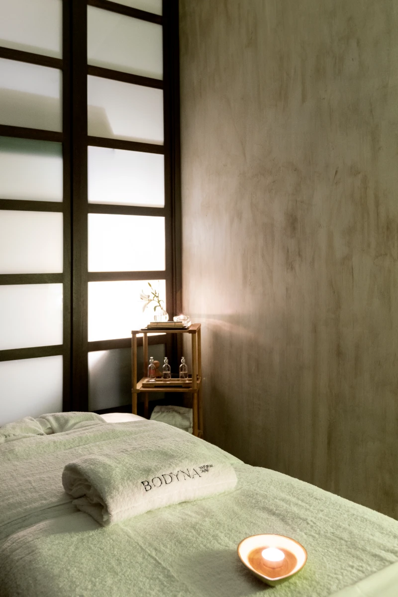 Habitaci&oacute;n con cama verde, luz c&aacute;lida y ventana con rejas de madera