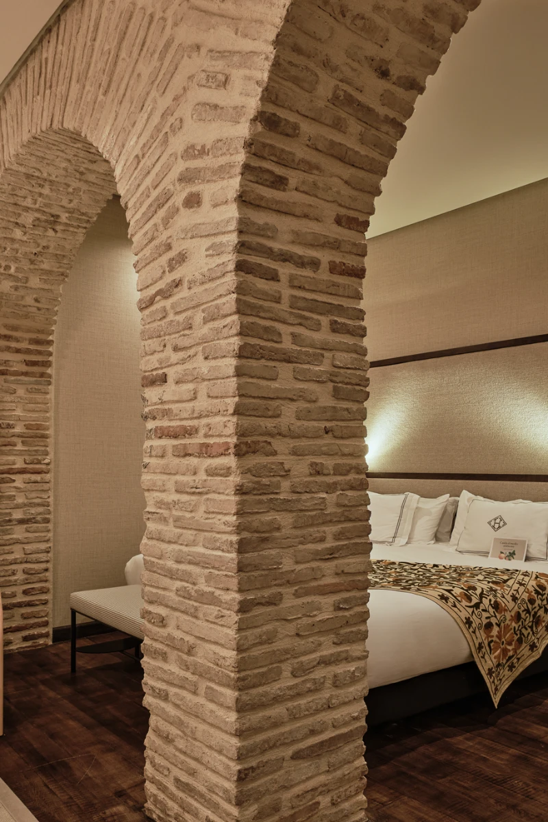 Interior hotelero con columnas de ladrillo y cama con cojines junto a la pared