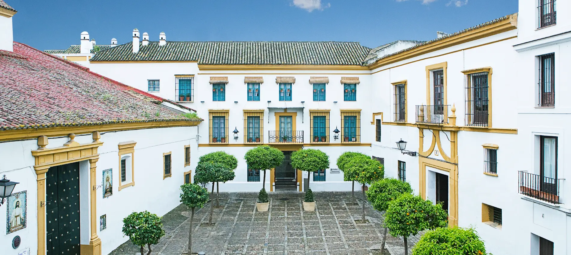 Patio andaluz con patio empedrado, &aacute;rboles verdes y casas blancas con tejados