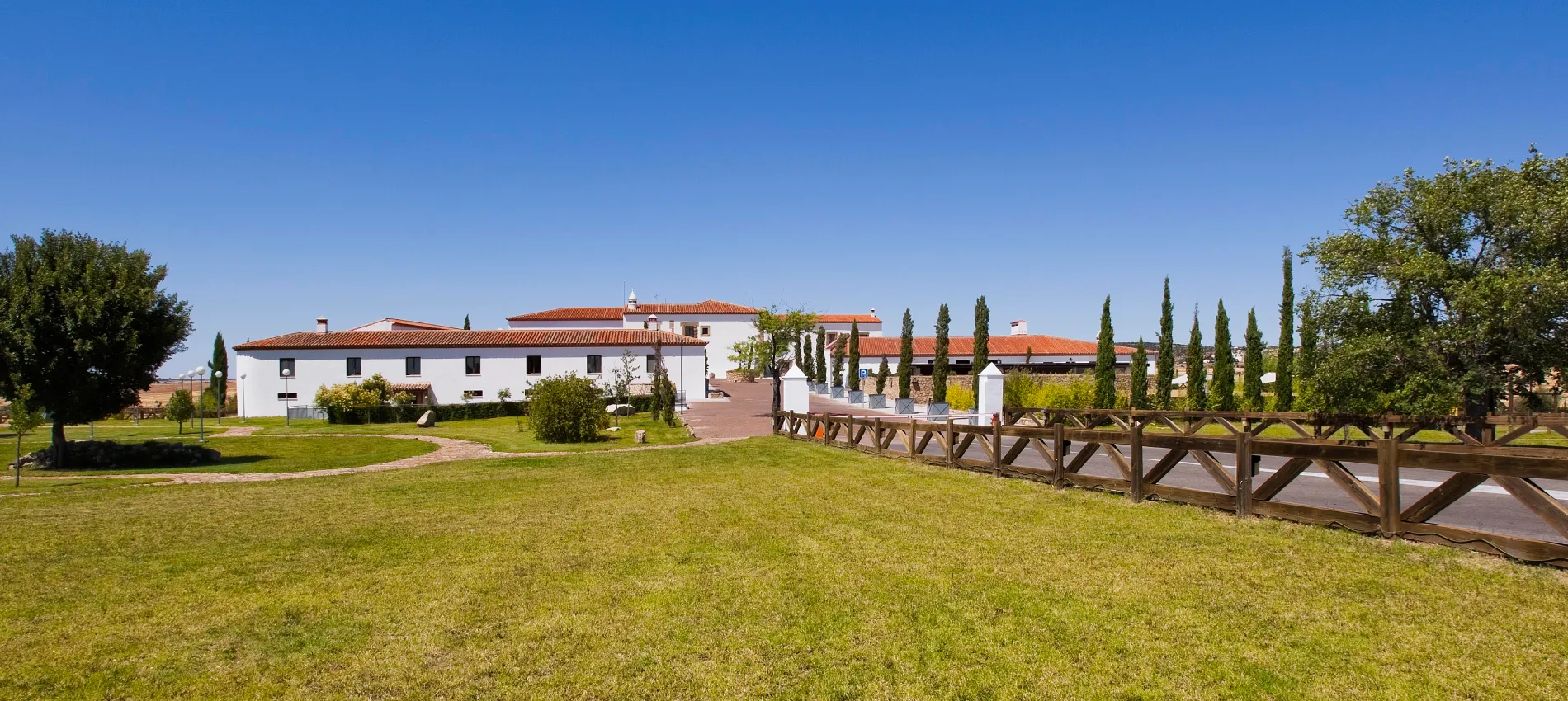 Vista exterior de una casa blanca con jard&iacute;n y camino de madera al cielo azul