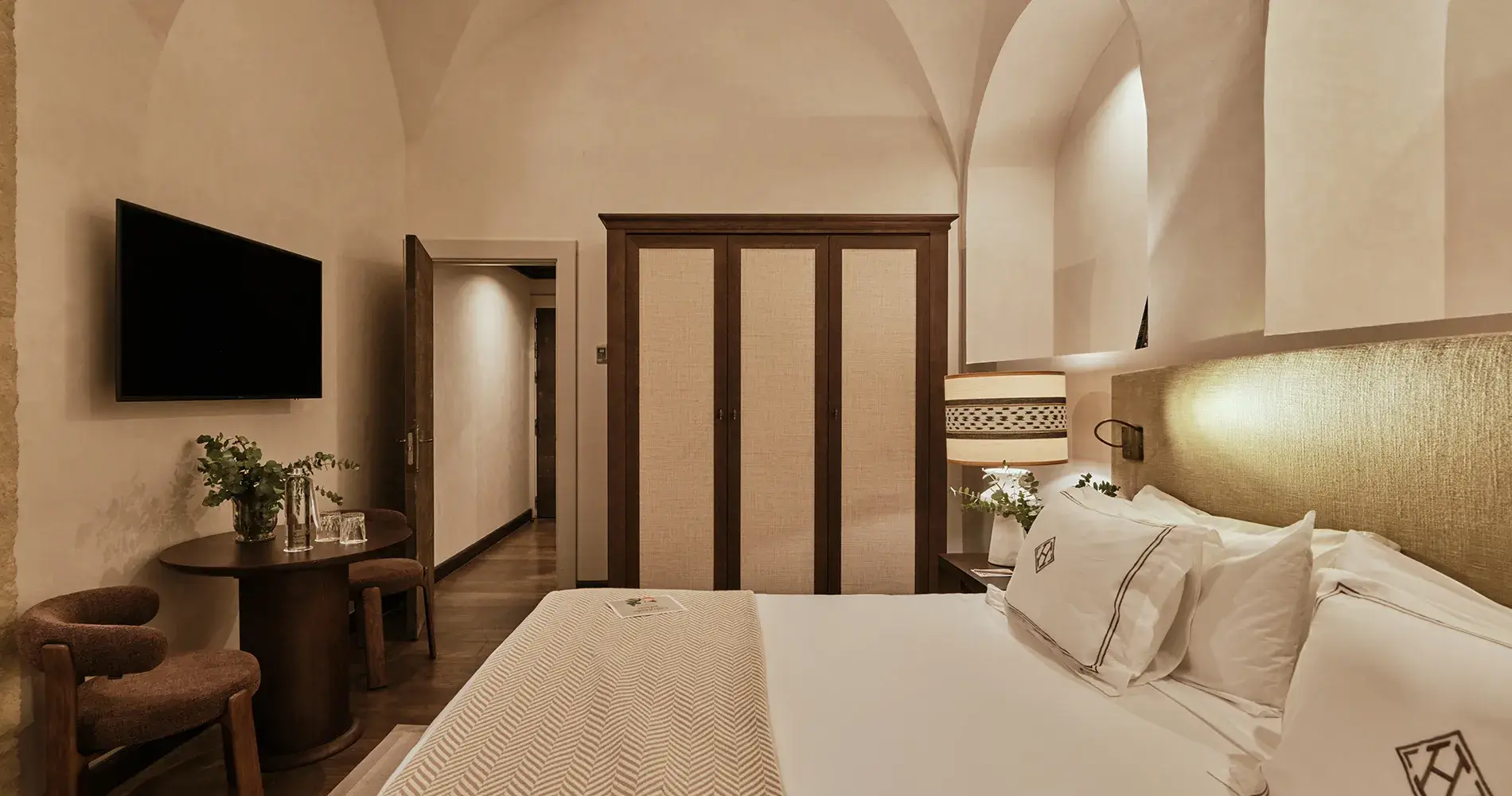 Habitaci&oacute;n de hotel con cama, sill&oacute;n y armario de madera, TV y mesa decorativa