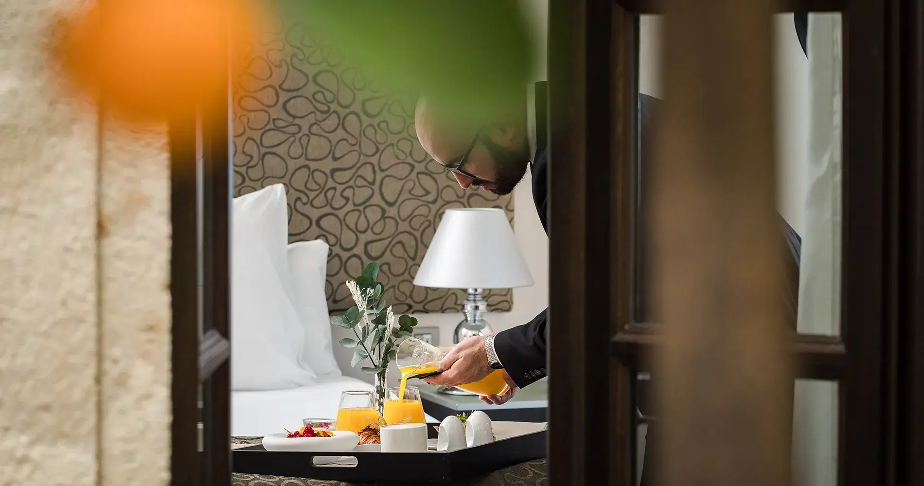Camarero sirve jugo de naranja a un desayuno en hotel, desde la habitaci&oacute;n