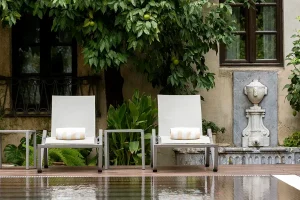 Terrace with two white armchairs, plants, and a fountain ornament near a wall