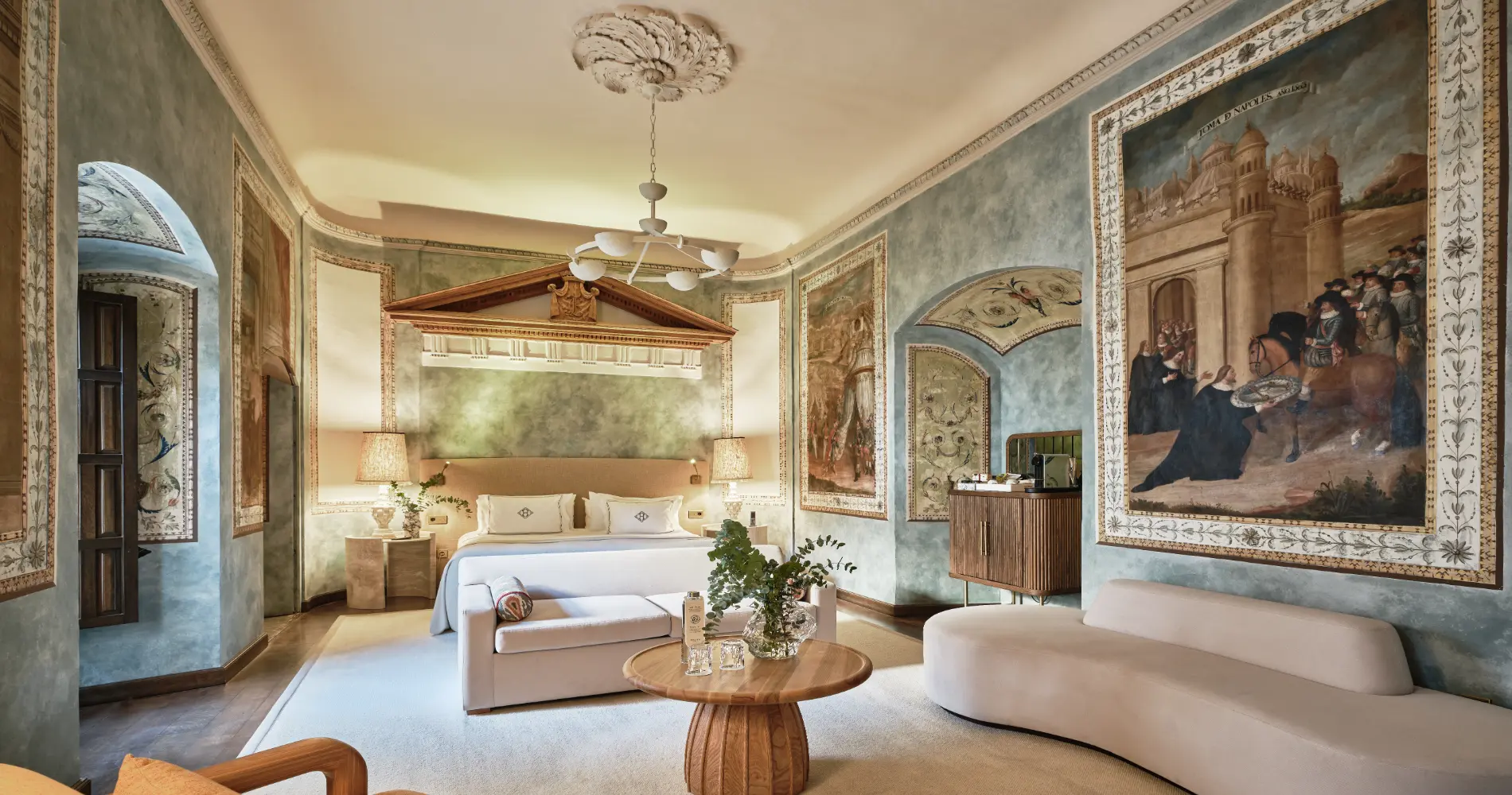 Suite hotelera elegante con cama, sof&aacute;, decoraci&oacute;n cl&aacute;sica y l&aacute;mparas modernas