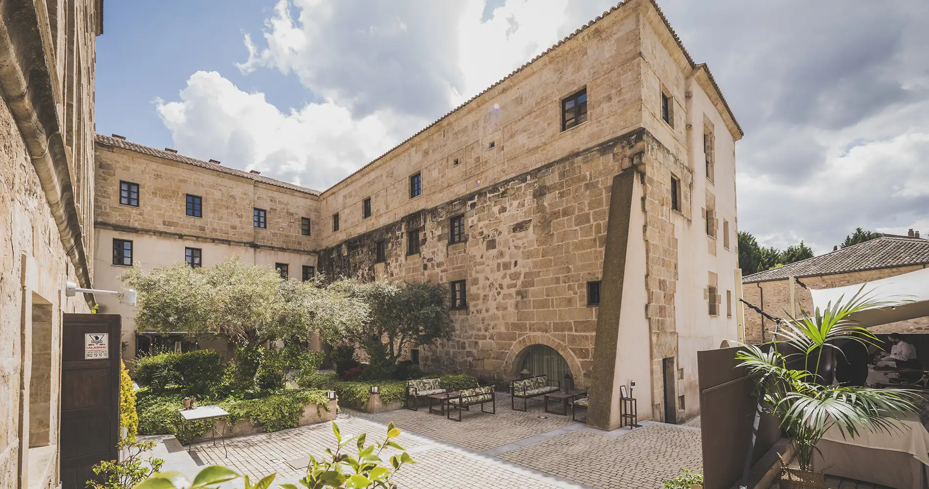 Patio con edificio de piedra y terraza, cielo nublado y jard&iacute;n interior