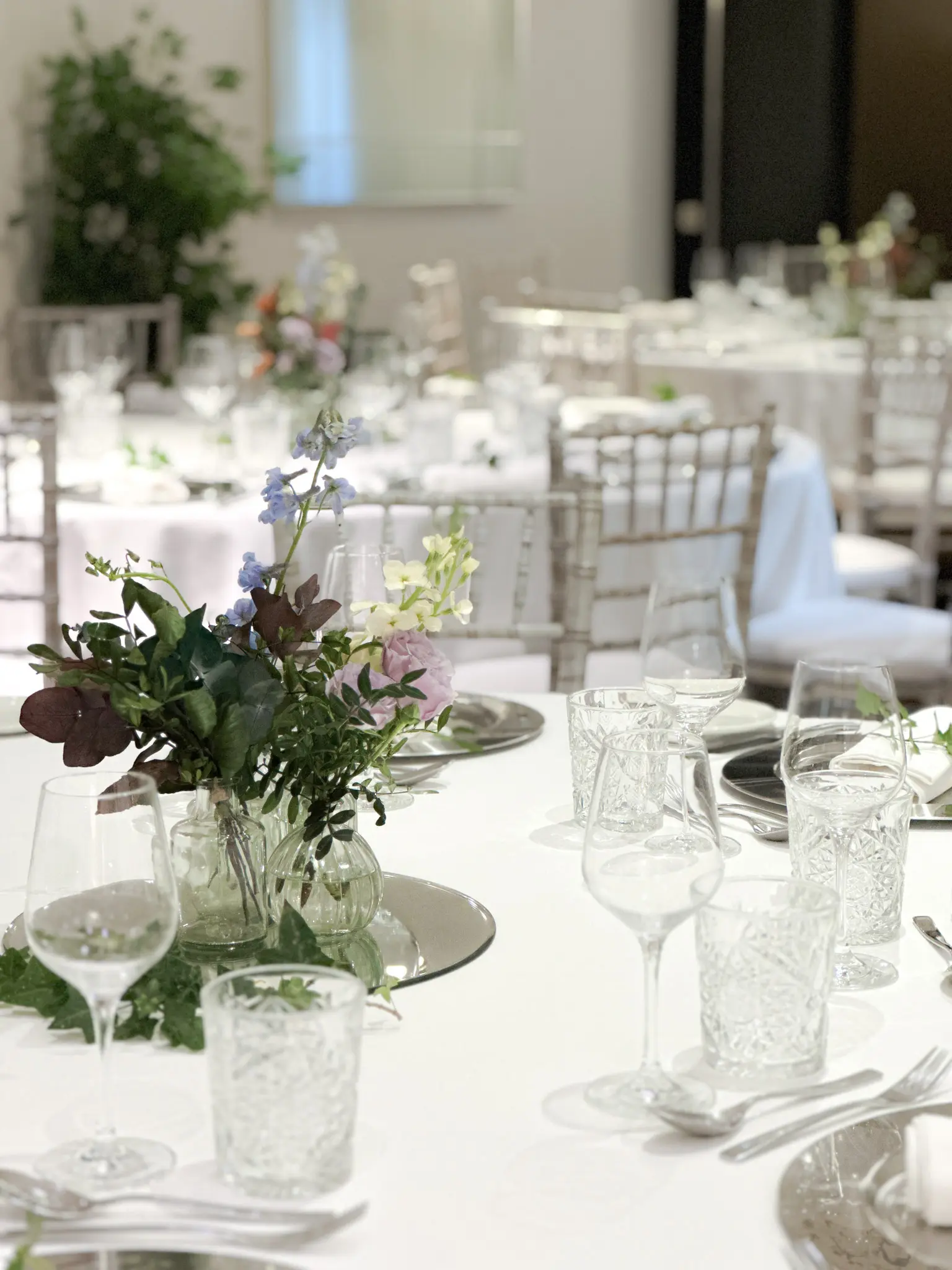 Mesa de banquete con arreglos florales y sillas blancas al fondo