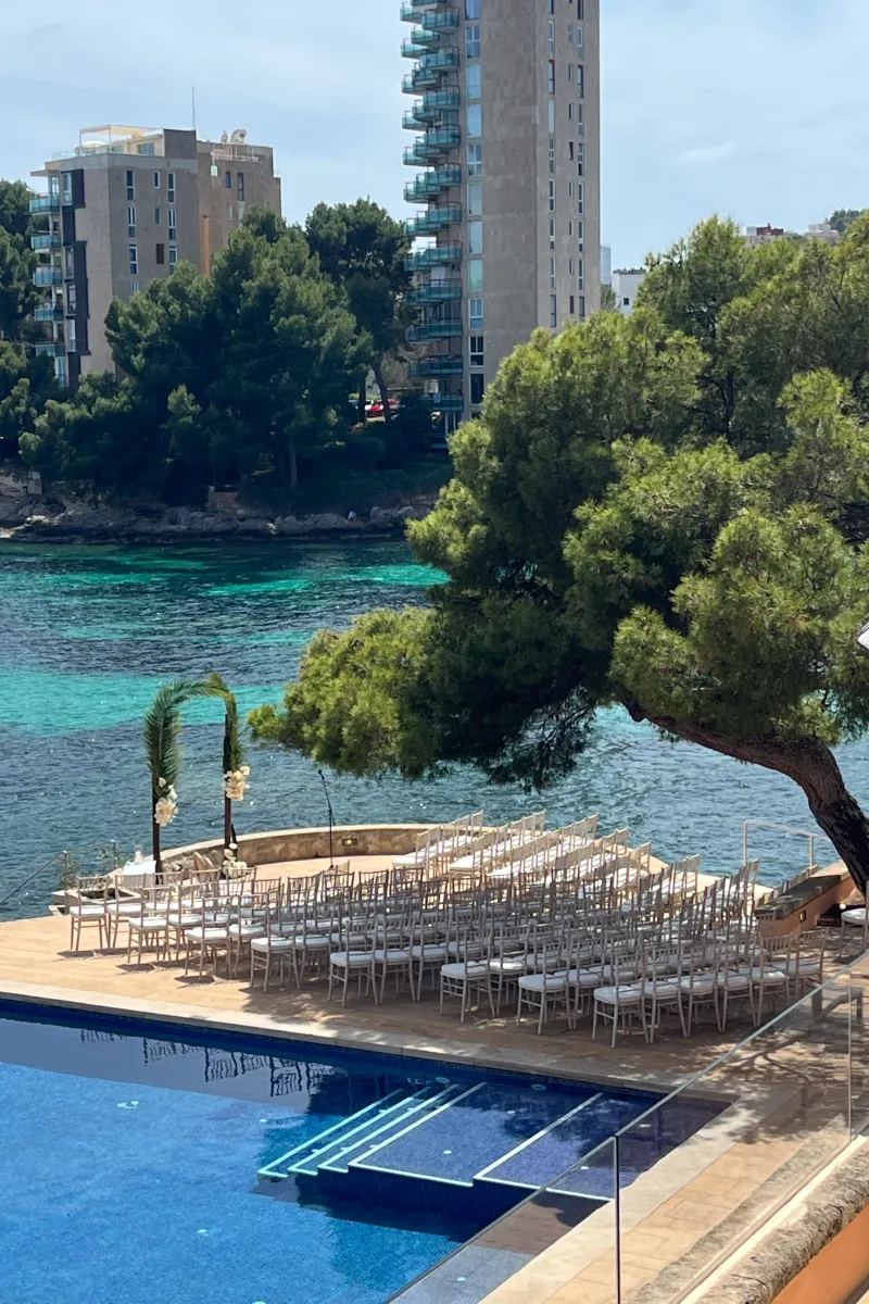 Ceremonia al aire libre junto a piscina y sillas blancas, mar y edificios altos