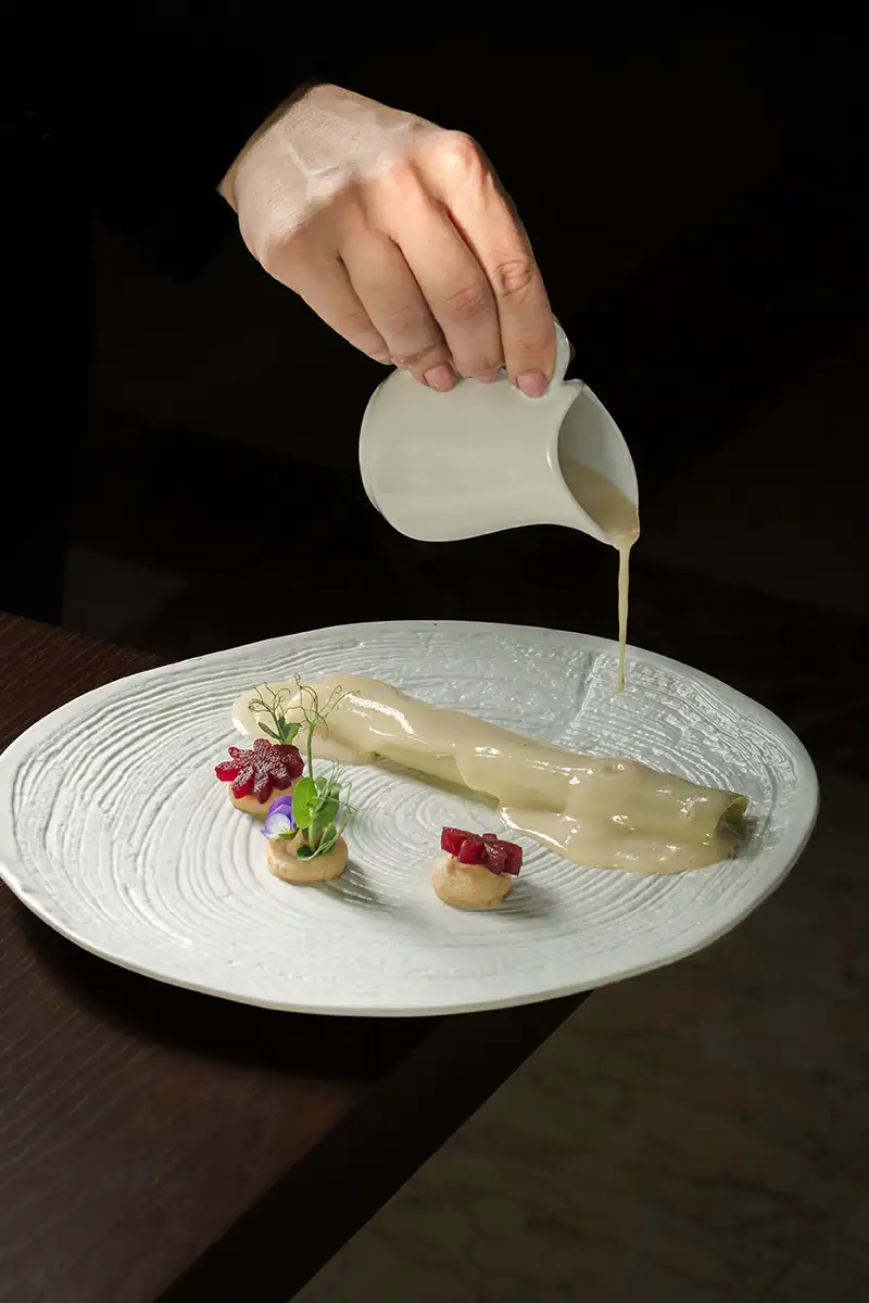 Mano sirve salsa cremosa sobre un plato con decoraci&oacute;n gourmet