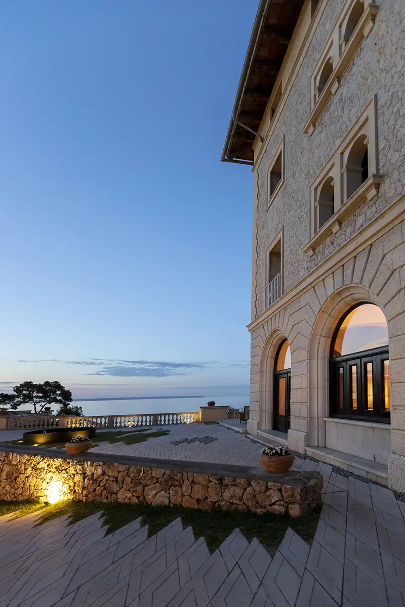 Fachada hist&oacute;rica con arcos y jard&iacute;n junto al mar al atardecer