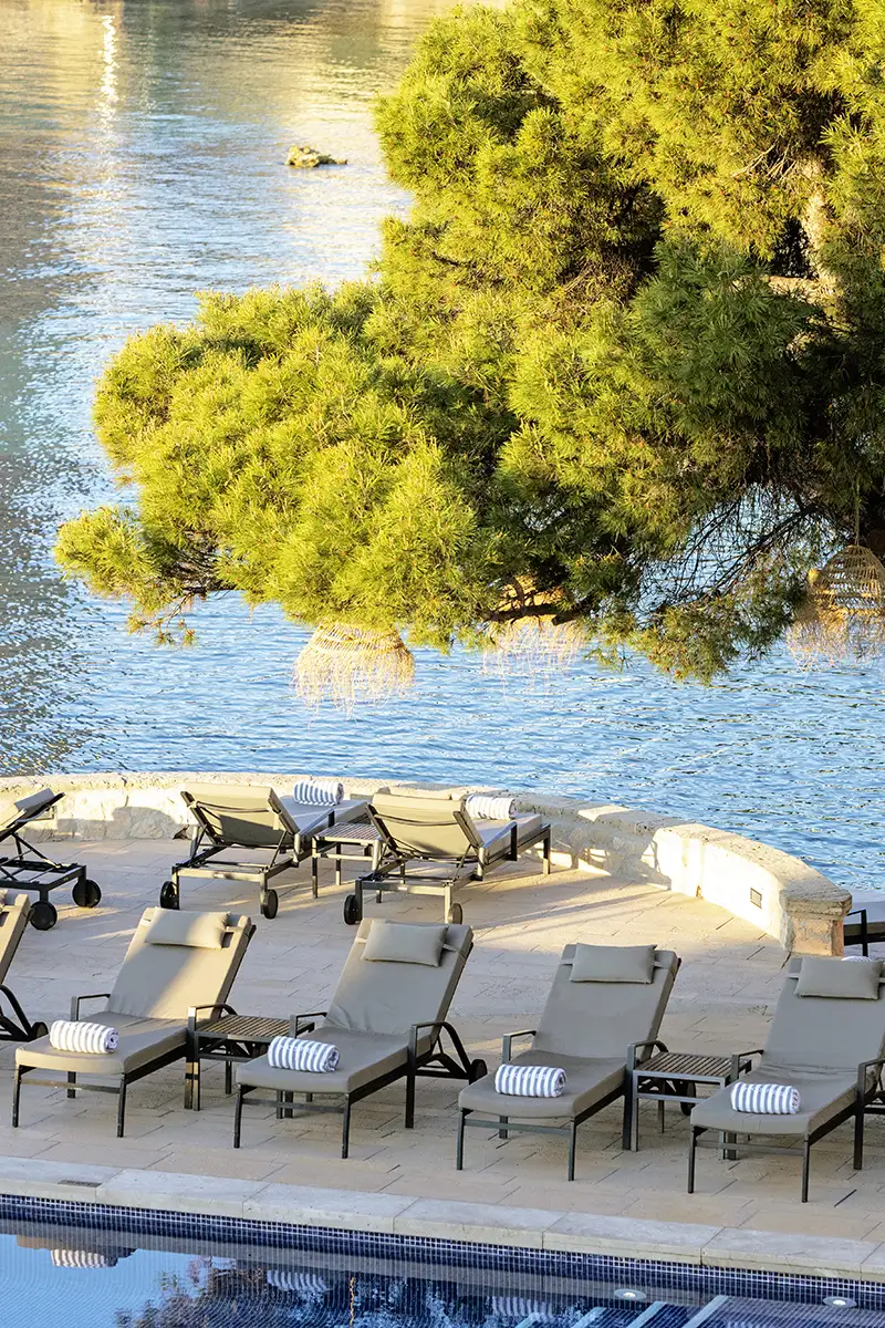 Terraza con camastros junto a piscina y &aacute;rboles verdes sobre el r&iacute;o