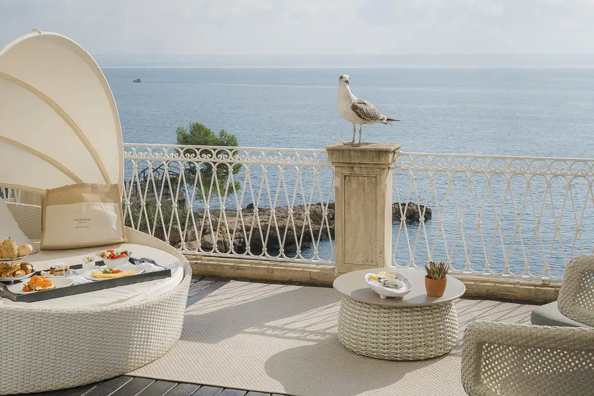Gaviota de pie en columna, terraza frente al mar con muebles y mesa