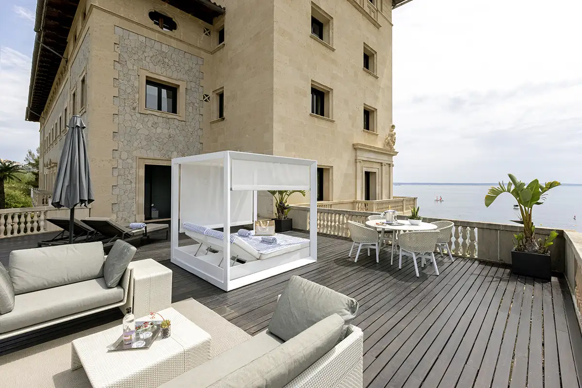Terraza junto al mar con muebles blancos y cama c&uacute;pula transparente en hotel
