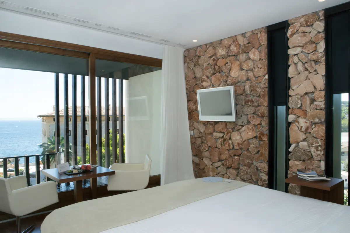 Interior moderno con dormitorio, pared de piedra y vista al mar por ventanales