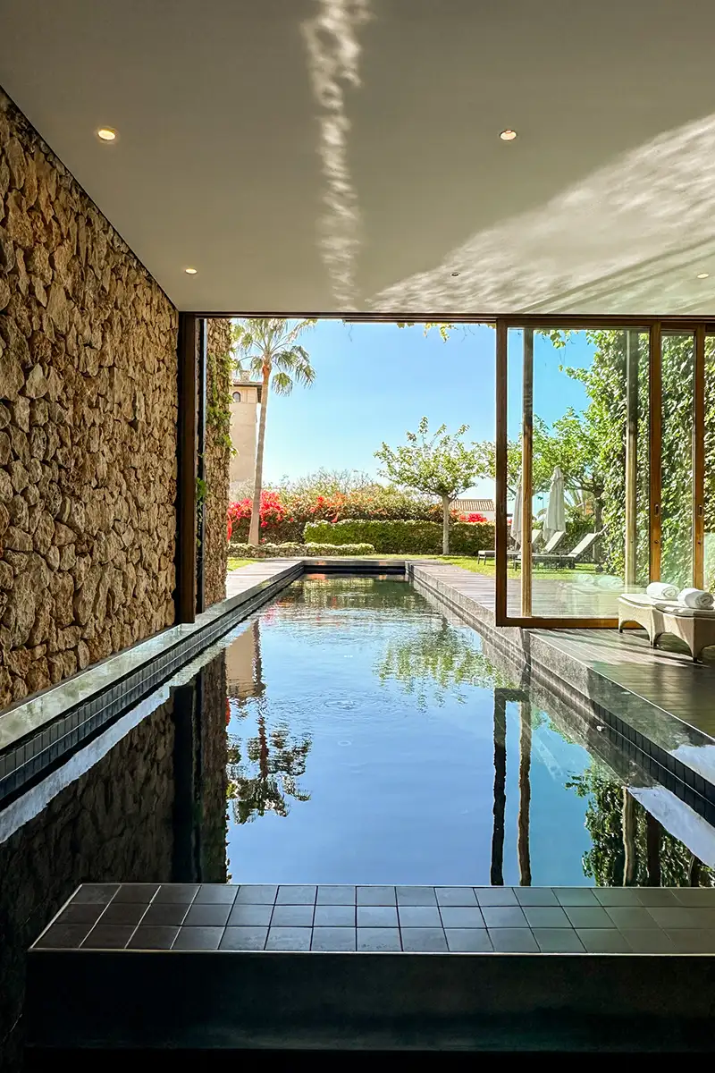 Piscina interior con jard&iacute;n y palmeras, luz natural y cielo azul al fondo